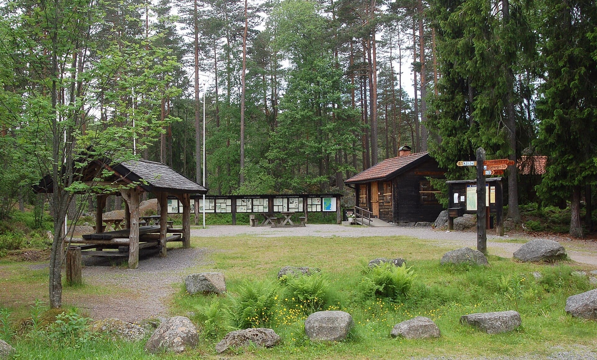 Rastplats i Tivedens nationalpark med vindskydd, informationstavlor, en timrad stuga och en vägvisare mot Trollstigen och Oxaberget.