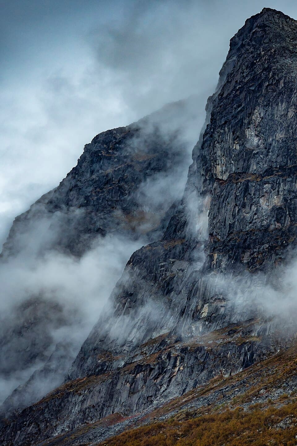 Dramatisk klippvägg i Stora Sjöfallet/Stuor Muorkke nationalpark, delvis dold i moln och dimma.