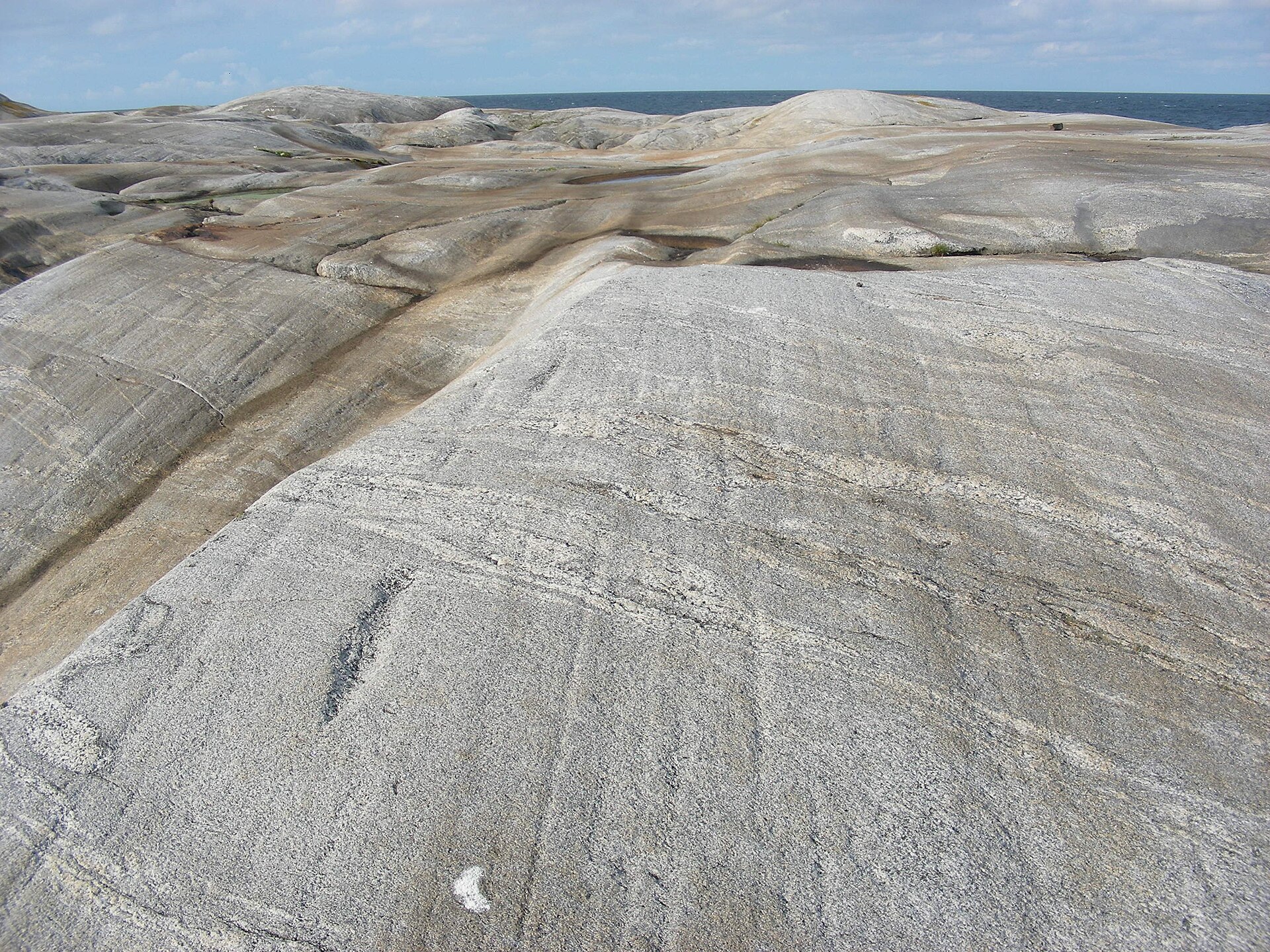 Glacialt slipad och räfflad granithäll vid havet i Kosterhavets nationalpark, med tydliga isräfflor i berget och havet synligt i bakgrunden.